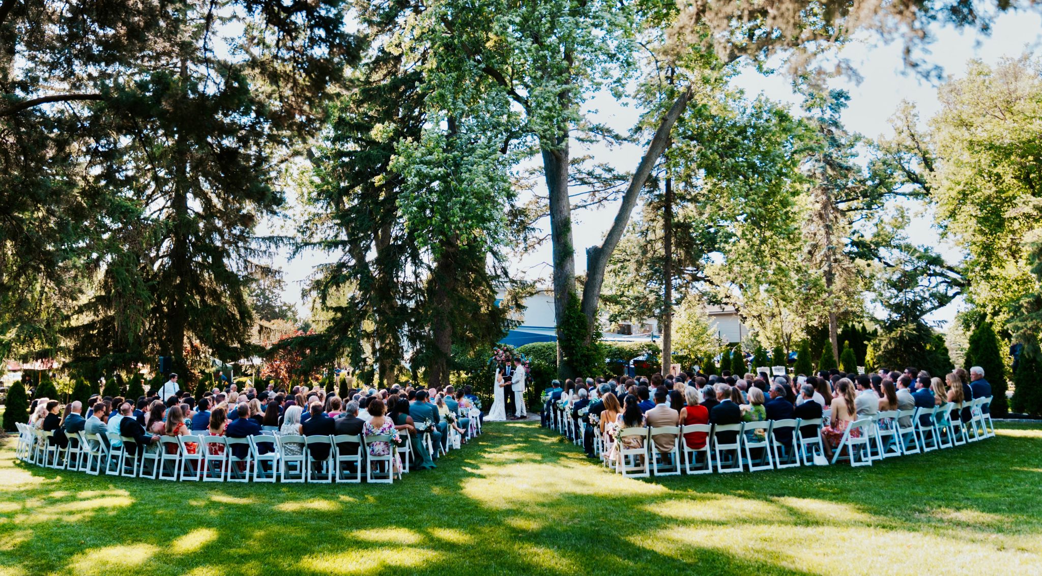 An outdoor wedding ceremony on the lawn beneath mature oak trees