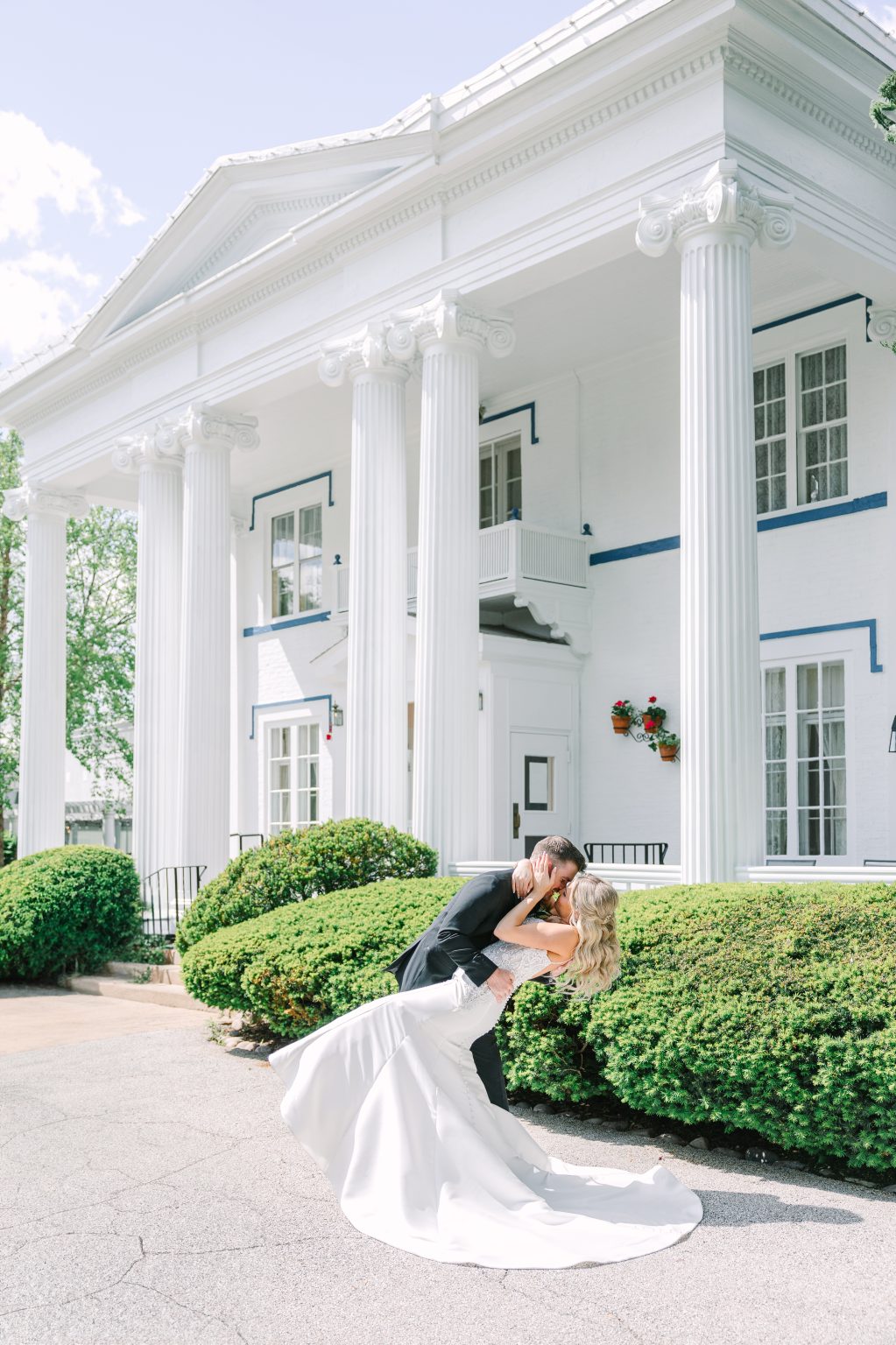 A couple dipping for a kiss in front of the mansion's white columns