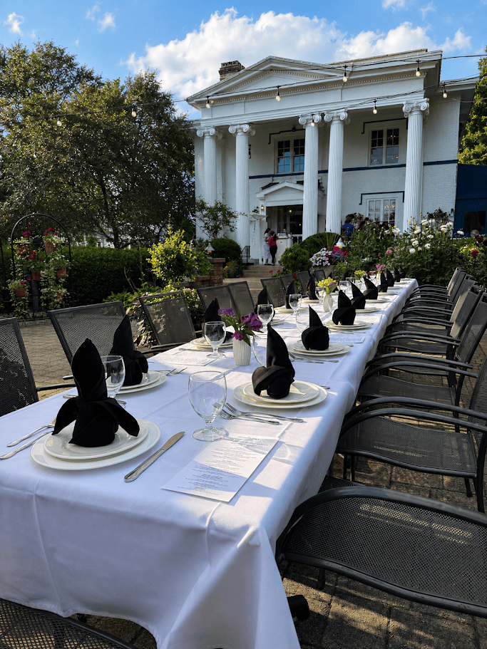 A long table set for dinner on the columned front veranda of the mansion